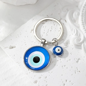 Silver evil eye keychain with blue concentric glass charms on a textured white surface