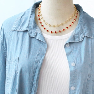 Detail of double-layer gold necklace featuring red and white heart-shaped charms