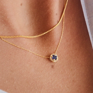 Detail of gold clavicle necklace featuring a sapphire pendant with diamond halo
