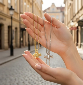 Detailed close-up of 18K gold plated bee pendant necklaces held against city background