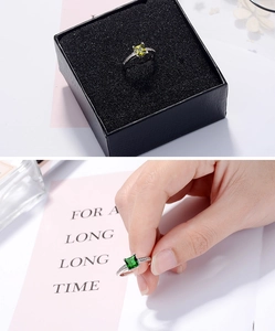 Close-up of square green zircon ring in a black gift box and held on a finger