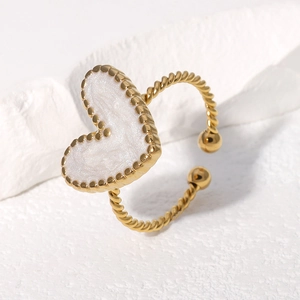 Detailed close-up of golden twisted heart ring with white enamel on stone background