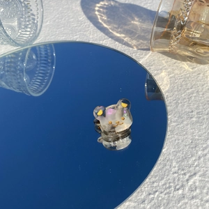 Détail d'une mini pince à cheveux ours en acétate reflétée sur un miroir bleu