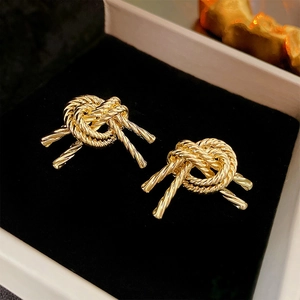 Macro shot of gold knot earrings featuring metallic rope texture on black velvet background