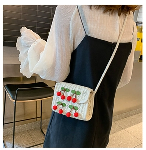 Detail of white straw square crossbody bag featuring 3D cherry accents and thin strap