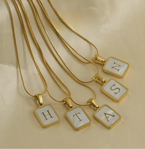 Macro detail of 18K gold plated square shell initial pendant on snake chain
