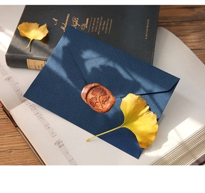 Detail of vintage navy blue linen textured envelope with bronze ginkgo leaf wax seal