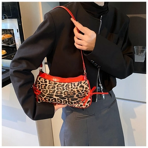 Chic leopard print shoulder bag with red patent leather trim worn by a model in a cafe