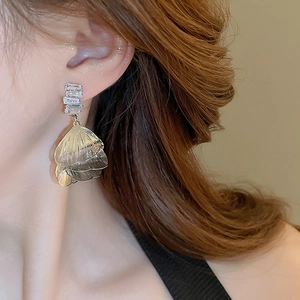 Detail of gold layered leaf drop earrings with baguette zircons worn by model