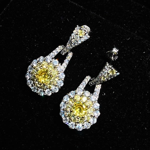 Macro shot of teardrop yellow crystal earrings with zircon accents on black velvet background