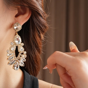 Close-up of golden teardrop tassel earring with sparkling crystals on a female model