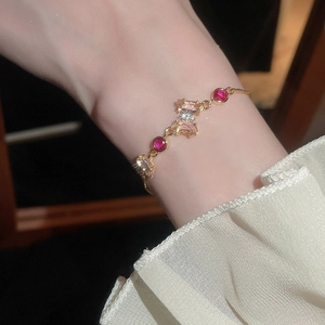 Détail d'un bracelet papillon doré avec zircons roses porté au poignet d'une femme