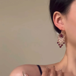 Vue détaillée de boucles d'oreilles ethniques avec gemmes rouges et pompons sur modèle