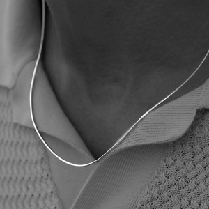 Minimalist silver flat snake chain necklace worn on a textured knit polo shirt for men