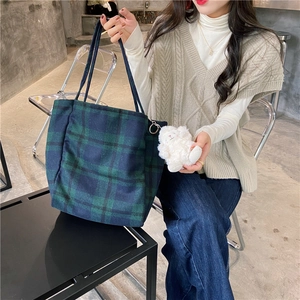 Green plaid wool tote bag with fluffy lamb charm shown in a lifestyle cafe setting
