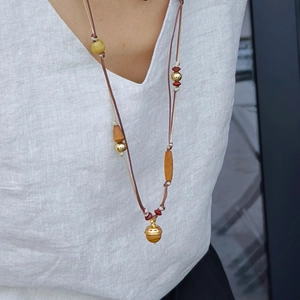 Détail de collier bohème avec perles en bois, corde tissée et pendentif cloche dorée