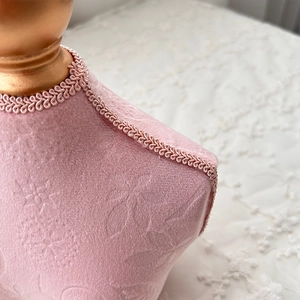Close-up of pink textured velvet jewelry bust with golden top and woven lace trim