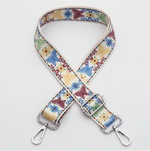 Close-up of beige woven bag strap with colorful butterfly embroidery and silver buckles