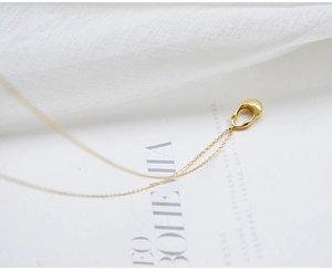 Macro shot of gold teardrop necklace on white textured fabric and magazine background