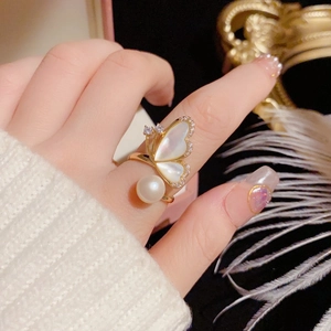 Détail d'une bague dorée ajustable avec papillon en nacre, perle et accents de zircone