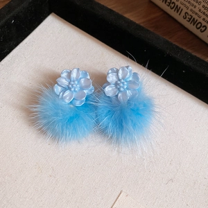 Close-up of blue resin flower earrings with soft fluffy round fur balls on display