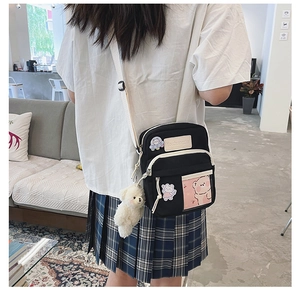 Vue latérale du sac bandoulière en toile noire avec broderie ours et breloque en peluche