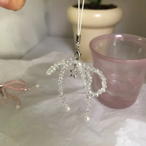 Macro detail of handmade crystal bow phone strap with mini pearls and star charm
