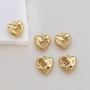 Close-up of five gold-plated heart charms for DIY jewelry making on a beige background