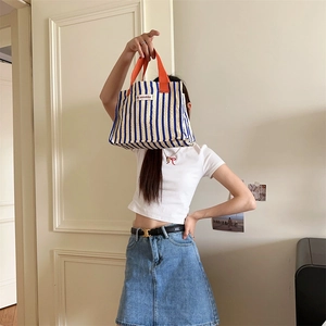 Detail of blue and white striped canvas tote bag with vibrant orange handles