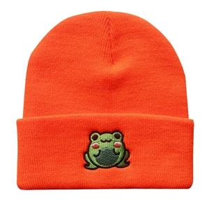 Macro shot of orange ribbed knit beanie showing detailed green frog embroidery and texture