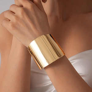 Gros plan d'un large bracelet manchette en métal doré poli avec une finition miroir