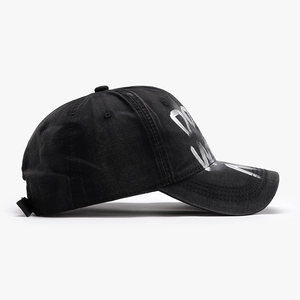 Distressed black cotton baseball cap with white graffiti letters shown from a side view