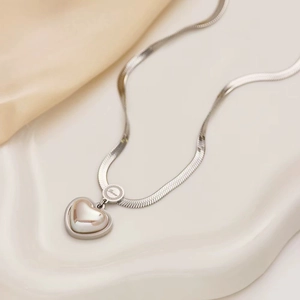 Silver snake chain necklace with pearl heart pendant on elegant beige silk background