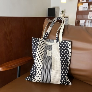 Borsa tote in tela a pois bianchi e neri esposta su un divano in pelle marrone