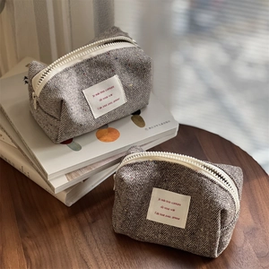 Chic herringbone tweed makeup pouch with top zipper on a rustic wooden tabletop