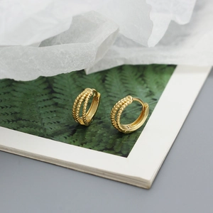 Macro shot of gold three-layer twisted weave huggie hoop earrings with soft lighting
