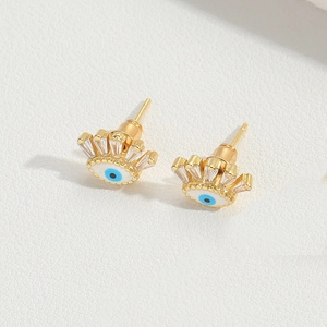 Close-up of golden evil eye stud earrings with blue enamel and radiant zircon stones