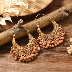Détail de boucles d'oreilles bohèmes en métal doré avec pompons en perles beige sur bois