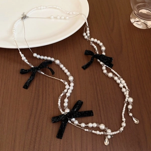 Detail of multi-layer pearl necklace with black velvet bows on a walnut wood surface