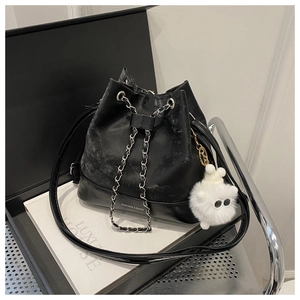 Detail of black textured bucket bag featuring chain strap and white monster plush charm