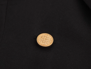 Close-up of golden embossed decorative button on black twill textured blazer dress