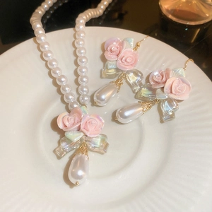 Detail of pink ceramic rose earrings and pearl necklace with iridescent bow pendants