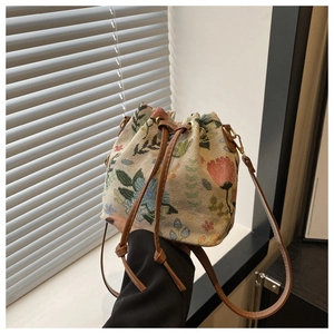Detail of floral embroidery on beige fabric bucket bag with brown drawstring and gold hardware