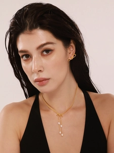 Détail d'un mannequin portant un ensemble collier et boucles d'oreilles nœud doré avec perles