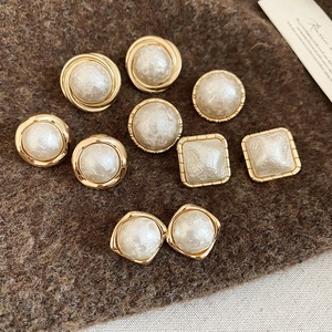 Macro view of gold plated geometric earrings with white pearl centers on brown felt background