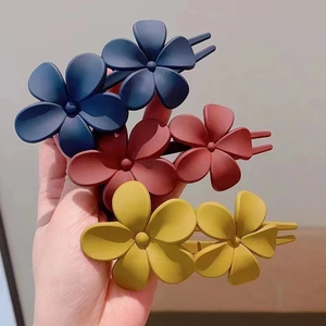Close-up of three matte plastic flower hair clips in navy blue, reddish brown, and mustard yellow