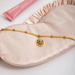 Detail of vintage gold stainless steel portrait necklace on soft pink silk fabric