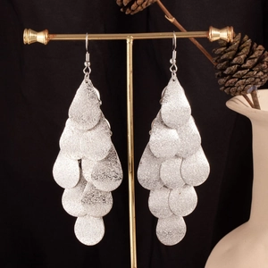 Macro shot of silver tiered teardrop earrings displayed on a gold stand with props