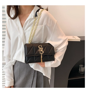 Close-up of black quilted shoulder bag with gold S-logo, tassel and chain strap detail