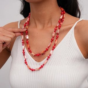 Detail of layered bohemian necklace with red beads and orange shell charms on a model